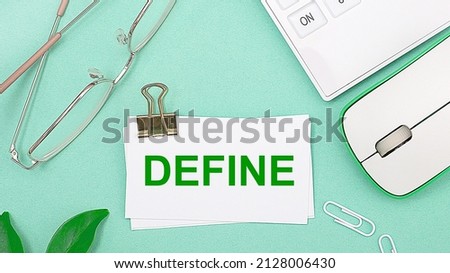 On a light green background there is a white calculator, a computer mouse, green leaves of a plant, gold-rimmed glasses and a white card with text DEFINE. Business concept