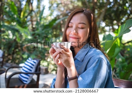 Portrait image of a young woman holding and drinking hot coffee in outdoors cafe