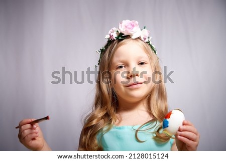 Pretty blonde little girl painting Easter eggs on white background