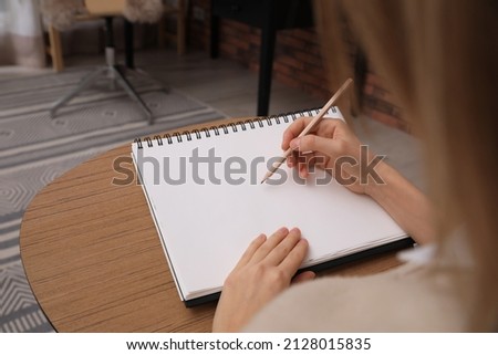 Woman drawing in sketchbook with pencil at home, closeup