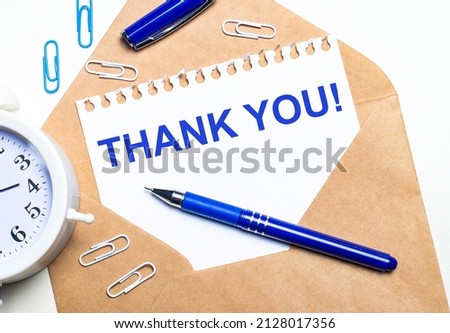 On a light background, a craft envelope, an alarm clock, paper clips, a blue pen and a sheet of paper with the text THANK YOU