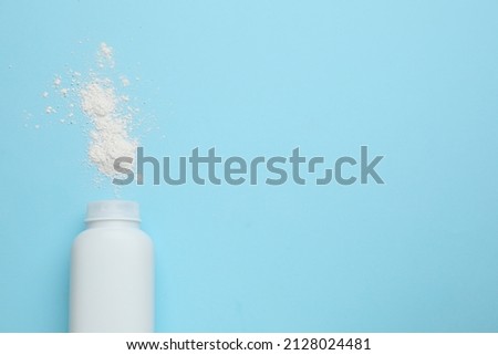 Bottle and scattered dusting powder on light blue background, top view with space for text. Baby cosmetic product Royalty-Free Stock Photo #2128024481