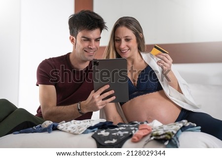 Young pregnant woman with her partner shopping online for the baby with a tablet