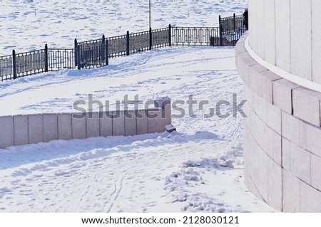 A fragment of the snow-covered city embankment of the Amur River. Winter morning. Metal and granite. Gentle descent and fence. Traces of people and animals on a white snow carpet.