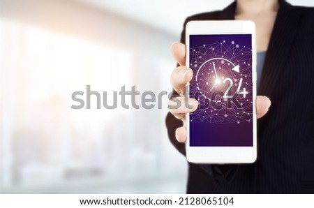 24 7 all day all night. Hand hold white smartphone with digital hologram 24 7 all day all night sign on light blurred background