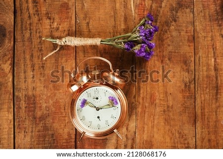 Vintage, beautiful alarm clock made from gold metal with blue flowers instead of clock's hands and small bouquet of flowers on wooding surface. Awakening. Spring time. Time for spring. Conceptual pic