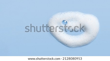 Soap cleanser foam texture. Children shampoo bubbles funny face on blue background. Cosmetic foamy cleansing product swatch  Royalty-Free Stock Photo #2128080953
