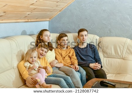 Five children sit on a leather sofa and watch TV.