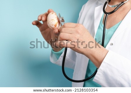 Doctor with stethoscope holding Easter painted egg in her hand on blue background, medicine