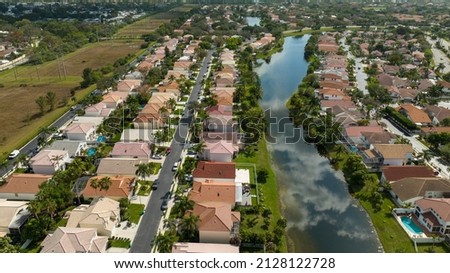 An aerial view high over a reflective pond, surrounded by beautiful houses in a residential neighborhood on a sunny day in Margate, Florida. Royalty-Free Stock Photo #2128122728