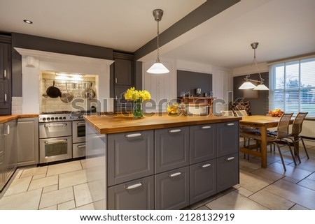 Modern kitchen with traditional looking built in cabinets in grey and white with built in range style oven and breakfast area with table and chairs Royalty-Free Stock Photo #2128132919
