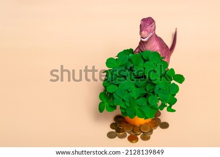 St. Patrick's day happy dinosaur, a bouquet of clover in a bucket and gold coins on a beige background. Close up with copy space