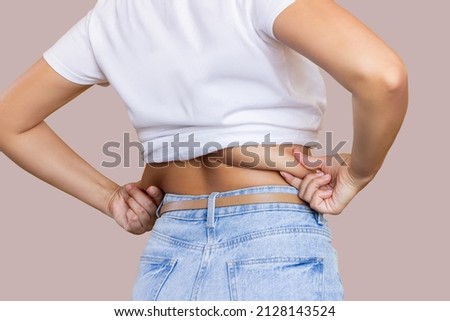 Behind back rear view photo of a young woman holding fat folds on her back isolated on color beige background. Overweight. Exercises for the back. Body positive