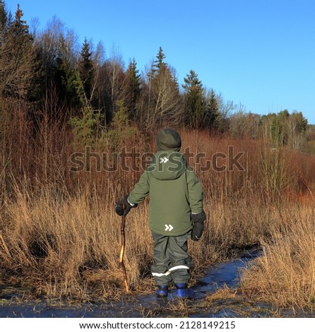 Boy with a stick in nature. Landscape photo during the month of February. Sunny and nice weather outside. Concept of exploring environment. Hat or cap. Stockholm, Sweden, Scandinavia, Europe.
