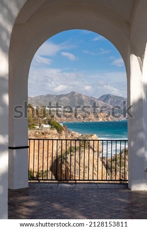 Beautiful landscape seen through an archway on Balcony of Europe , Nerja city, Malaga. View of La Chalaonda beach with Sierra Nevada mountains in background. Cloudy day. Vertical photography.