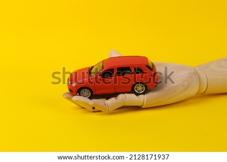 Wooden hand holding toy car model on yellow background