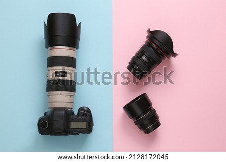 Professional digital camera with a set of lenses on a blue-pink background. Top view.