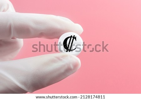 A hand in a medical glove holds a pill with a colon sign on a pink background. Expensive medicine in Costa Rica.