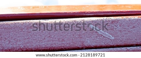 Red wooden bench top planks. Covered with frost and bright sunlight. Horizontal banner