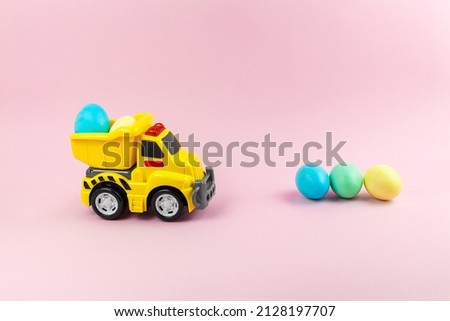 A toy yellow truck carrying Easter eggs in pastel colors. Easter card with place for text on a pink background. Easter food delivery