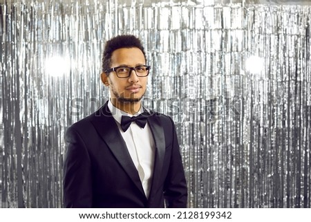 Portrait of young African American man in formal suit and glasses on glitter disco background. Profile picture of black male entertainer or mc in formalwear in discoclub or nightclub. Entertainment.