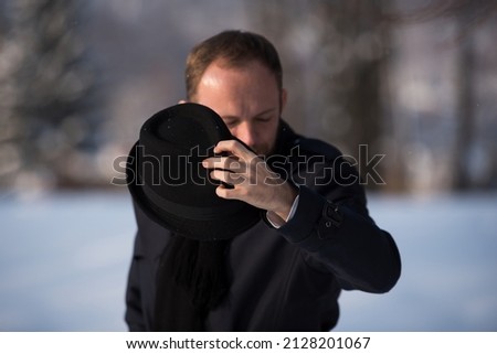 Close-up of a hand that smashes a hat. In the background a young man, winter landscape and sunny day.