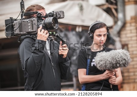 Behind the scenes. Cameraman shooting the film scene with camera on outdoor set. Photography director in movie filmmaking action