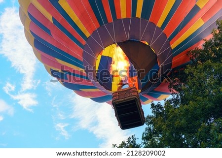 Colorful hot air balloon with people in a basket rises to the sky among the trees. Royalty-Free Stock Photo #2128209002