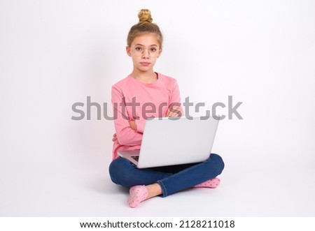 Confident Beautiful caucasian teen girl sitting with laptop in lotus position on white background with arms crossed looking to the camera