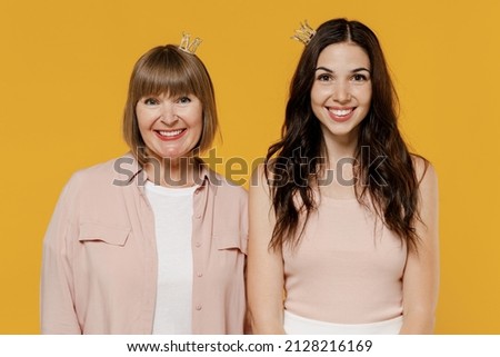 Two young smiling happy lovely daughter mother together couple women wearing casual beige clothes diadem party crown isolated on plain yellow color background studio portrait. Family lifestyle concept