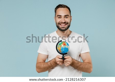 Young smiling happy geography teacher man 20s wear casual white t-shirt hold in hands Earth world globe isolated on plain pastel light blue color background studio portrait. People lifestyle concept