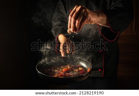 Cooking fresh vegetables. The chef adds salt to a steaming hot pan. Grande cuisine idea for a hotel with advertising space. Royalty-Free Stock Photo #2128219190