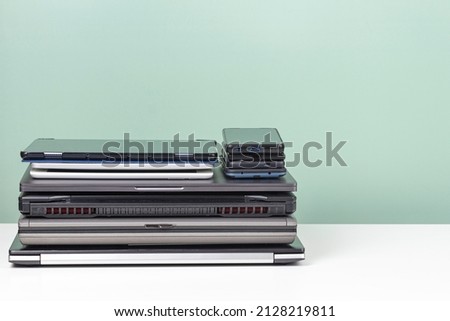 Pile of old used laptop computers, digital tablets, smartphones for recycling on white table. Planned obsolescence, e-waste, electronic waste for reuse and recycle concept Royalty-Free Stock Photo #2128219811