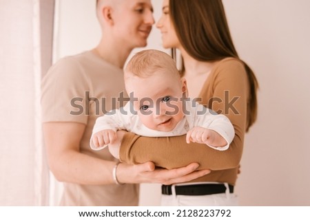 Stylish young family, photographed with a little beautiful baby. The family expresses love and awe to each other. Family and parenting concept.