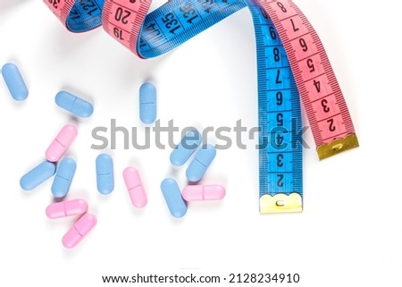 Pills with pink and blue measuring tape on white background. Concept of losing weight, diet, fat burning, healthy eating. Copy space.
