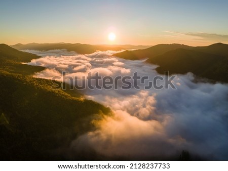 Aerial view of foggy evening over dark pine forest trees at bright sunset. Amazingl scenery of wild mountain woodland at dusk Royalty-Free Stock Photo #2128237733