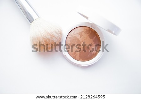 A white pillbox with powder and bronzer lies on a white background, next to it lies a brush for blush. High quality photo Royalty-Free Stock Photo #2128264595