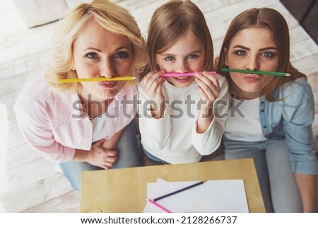 Top view of happy beautiful granny, her daughter and granddaughter posing with colorful pencils and looking at camera