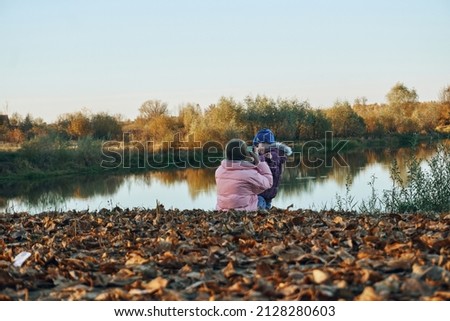 Two sisters take pictures of each other, posing for a camera, autumn leaves, a lake, a river. Photo shoot on the shore of the reservoir.