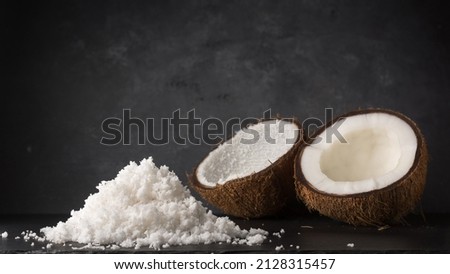 pile of scraped or desiccated coconut with two halves of coconut shell, healthy tropical fruits on a black surface, dark textured background with copy space Royalty-Free Stock Photo #2128315457
