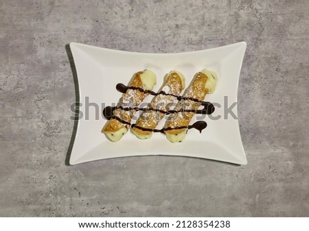 Three cannolis with chocolate chip filling and drizzled with chocolate syrup.