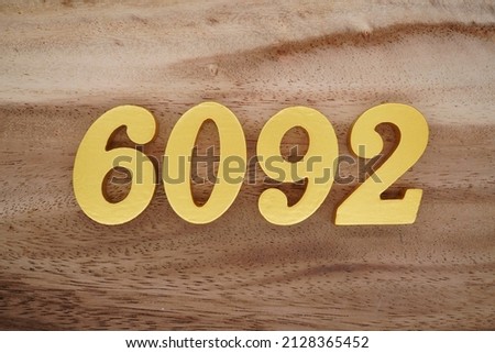 Wooden numerals 6092 painted in gold on a dark brown and white patterned plank background.
