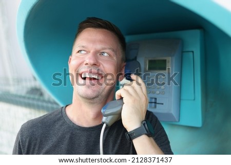 Happy man speaks on a public payphone on the street, close-up. Lack of mobile connection, phone call in the countryside Royalty-Free Stock Photo #2128371437