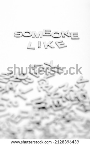 The phrase "Someone like you" is composed of little wooden letters and randomly letters in a pile on a white background. An abstract idea that will be proven in motivational words. BW photo.