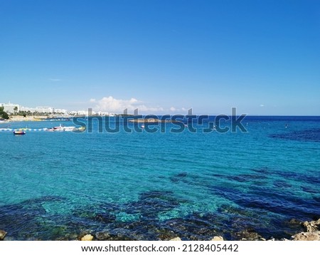 View of the clear water of the Mediterranean Sea, the pier on the Fig Tree Bay beach with a boat and catamarans and the island.