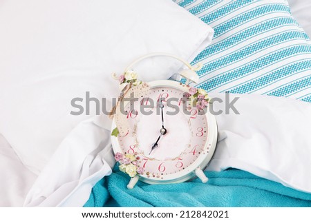 Metal clock on blue pillows on a big white bed