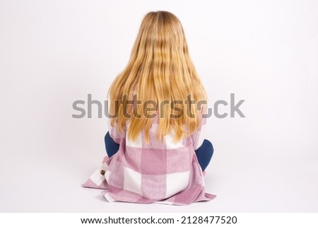 Beautiful caucasian teen girl sitting with laptop in lotus position on white background standing backwards looking away with arms on body.