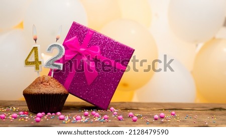 Happy birthday with a pink gift box for a 42 year old woman. Beautiful birthday card with a cupcake and a burning candle number forty two