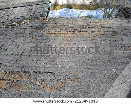 A shot of a rooftop with lots of missing shingles. The roof is severely damaged, weathered, decaying, rotting, and in need of repair or replacement. Royalty-Free Stock Photo #2128491818