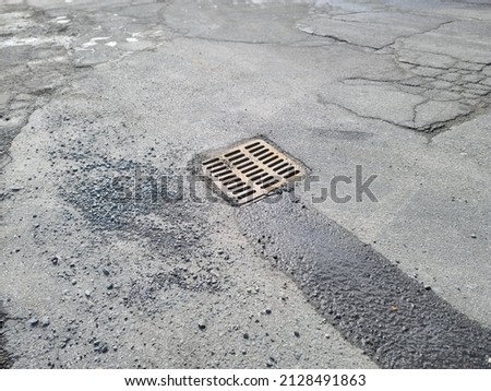 A drain in the middle of a cement area. The is a very shallow stream of water flowing into the drain grate.